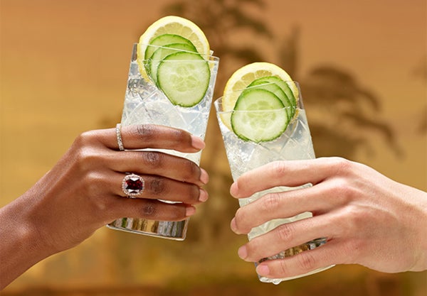 Two people holding drinks garnished with lemon and cucumber