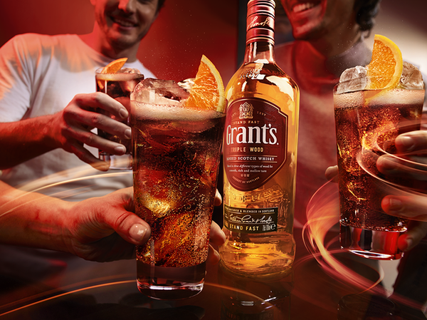 Three glasses of whiskey and cola held in the middle with a bottle of Grant's in the centre