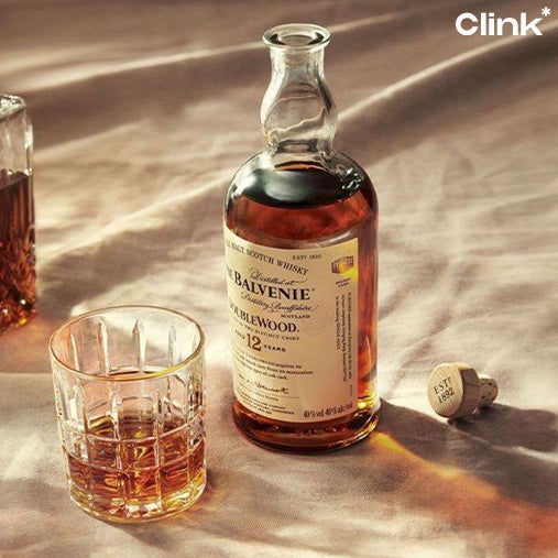 A whisky bottle is present with the cork placed beside it and a glass of it poured is located directly in front of it.
