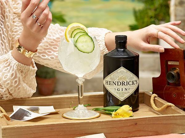 Bottle of Hendricks Gin with drink garnished with lemon and cucumber