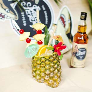 Heavily garnished pineapple being used as a glass with a bottle of Sailor Jerry