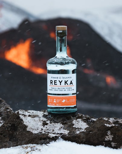 A bottle of Reyka vodka with ice in the foreground and fire in the background