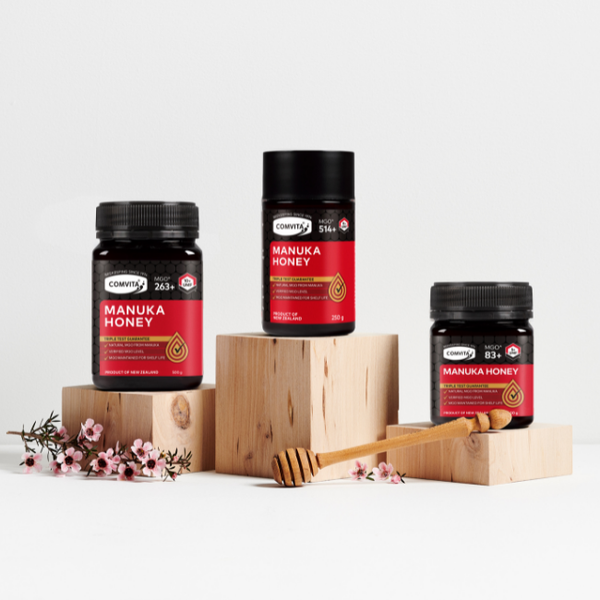 Different packages of Manuka Honey standing on small wooden stands. The composition is decorated with some flowers.