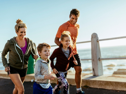 Genitori con due bambini - una ragazza e un ragazzo - che sorridono e mentre corrono sul lungomare durante un giorno soleggiato