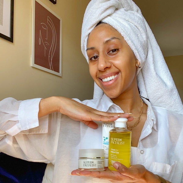 Woman with hair wrapped in a towel holding three different super facialist products. Visit Our Instagram