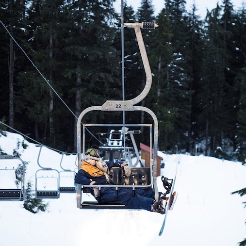 Visit Oneskee Instagram. Female snowboarder wearing our navy blue and mustard snowsuit on chairlift.