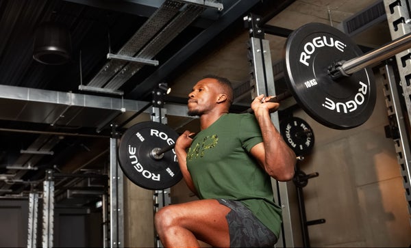 A man in a green camo MP gym clothing doing a barbell split squat workout in a gym.