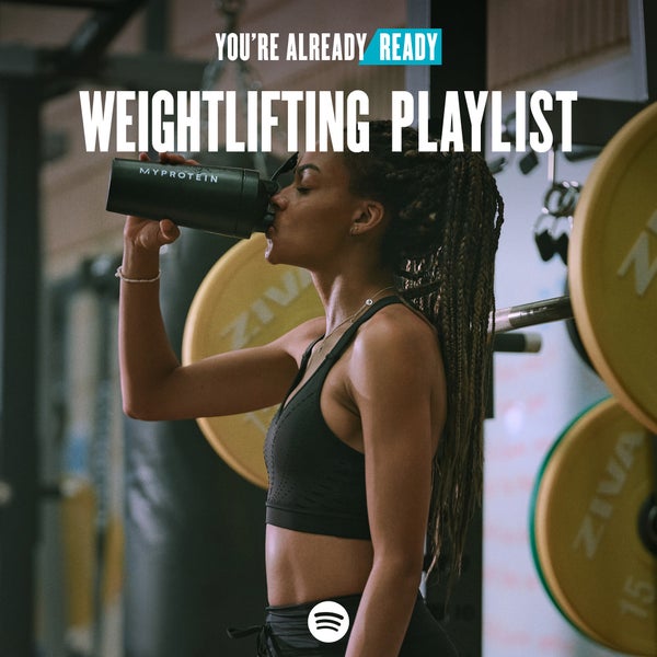 A woman wearing black workout clothes drinking from a black Myprotein shaker with the words 'You're Already Ready - Weightlifting Playlist' overlaying.