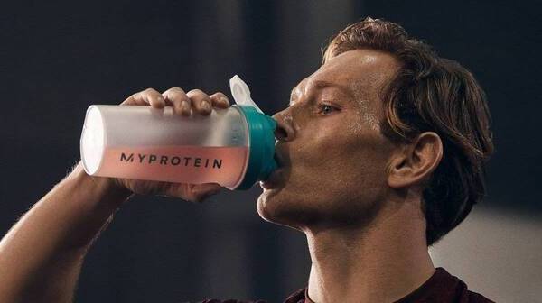 A person drinking an amino acid supplement from a Myprotein shaker at the gym.