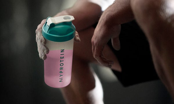 A person holding a Myprotein shaker with a pink liquid inside, representing the pre-workout range available from Myprotein.