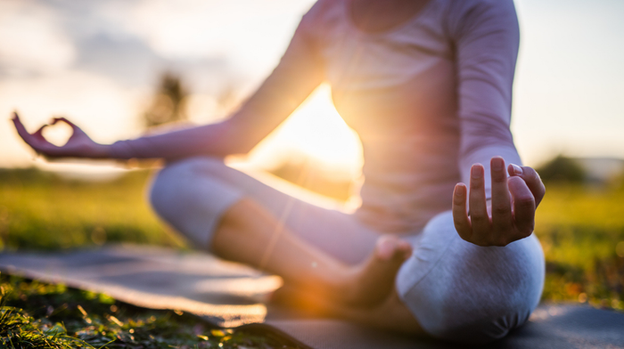 woman sat in mindfulness meditation pose with sunset in background