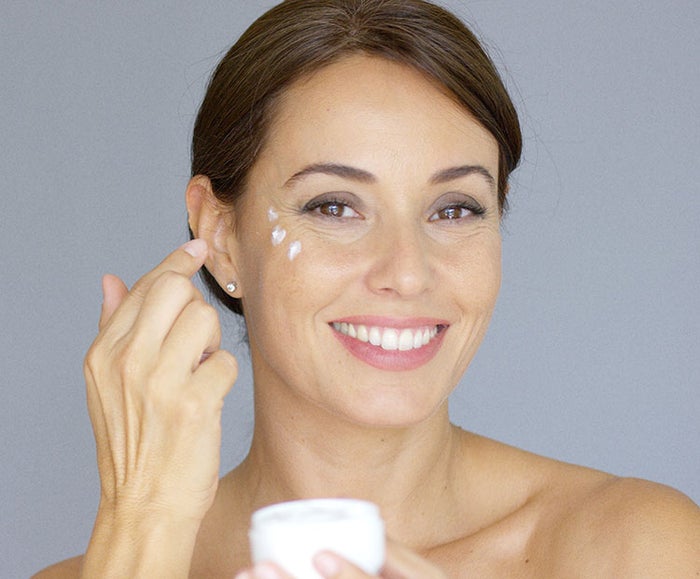 Woman applying eye cream on gray background 1