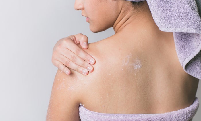 woman wrapped in towel applying lotion to shoulder