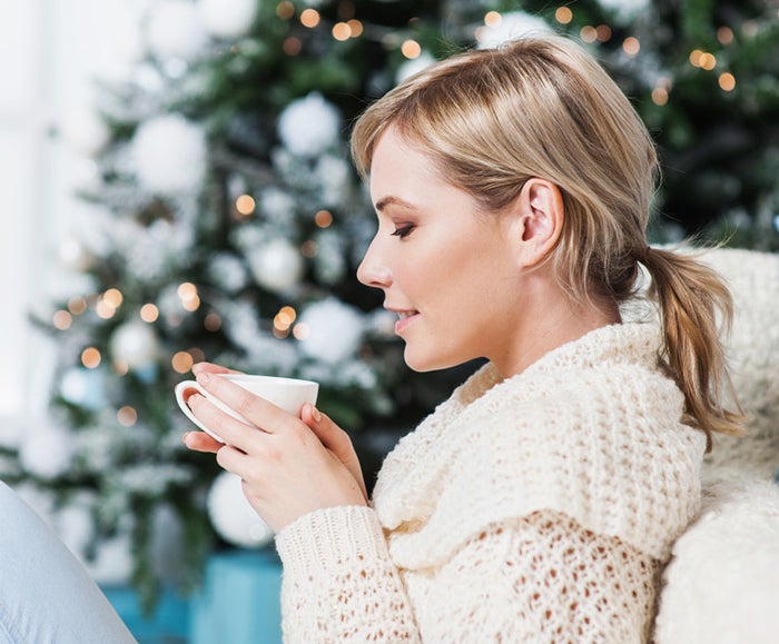 Woman sipping hot chocolate by christmas tree 1