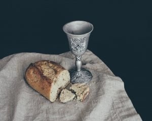 Pão e taça de vinho sobre toalha de linho em fundo escuro