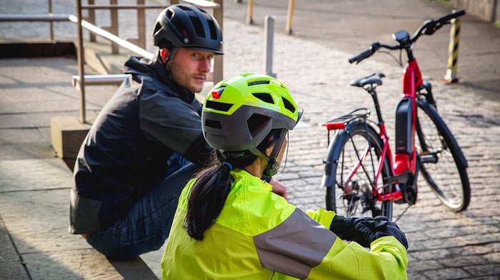 Two people sit next to bikes in high visibility jackets