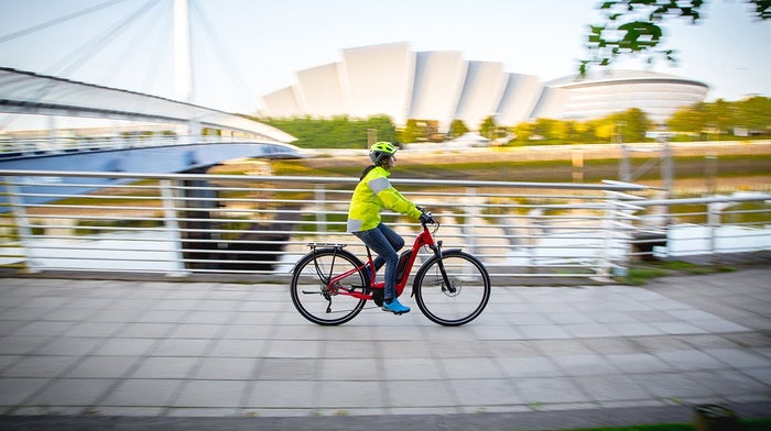 Woman cycles along quayside from left to right