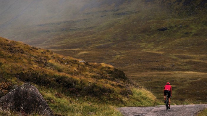 Person cycles down a road in the middle of grassy hills