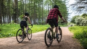   Two cyclists riding through a forest on a wide track 