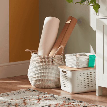 Woven basket with rolled up yoga mats in and a white plastic woven basket with smaller ones stacked on top.