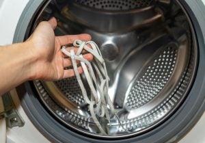 Someone placing their dirty shoelaces in a washing machine to be cleaned.