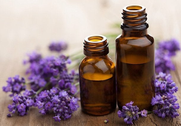 A wide shot of two small bottles of essential oils on a wooden table sat next to sprigs of purple lavender in an outdoor setting.