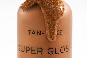 an open bottle of tan luxe gloss drops leaking out of the top all over the bottle