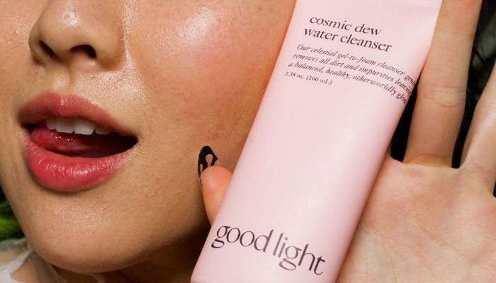 A close up of a woman's face as she holds a bottle of cleanser from Good Light