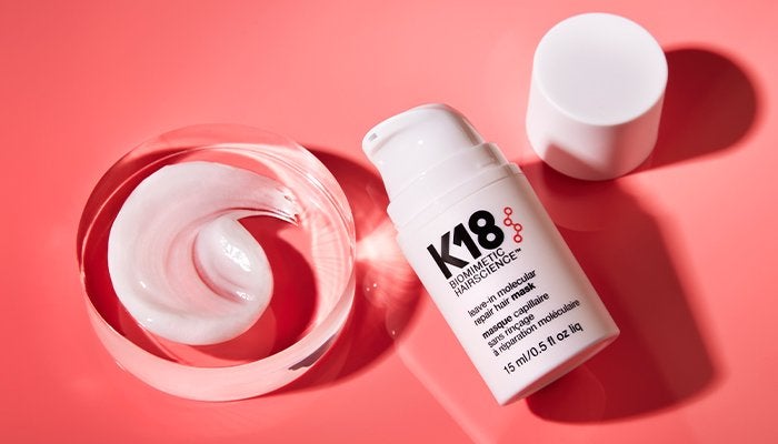 k18 haircare product against a rose background with a swirl of product nearby