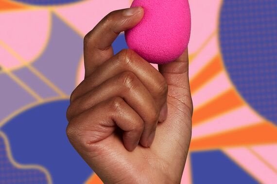 a hand holding a pink beautyblender against a multicoloured background