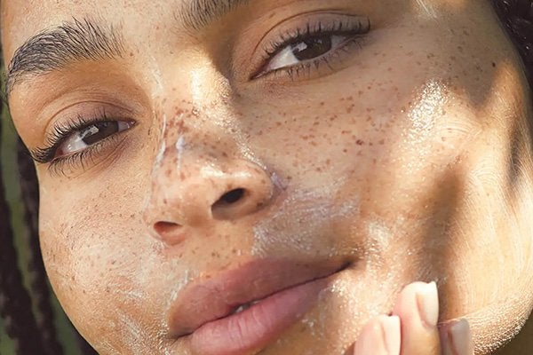 A close up shot of a female model with freckles applying a microbiome-protecting cleanser onto her face and rubbing it in.