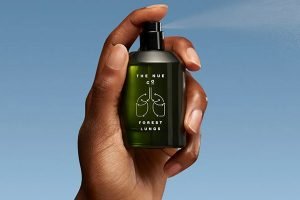 a dark skinned hand holding onto a green the nue co perfume spritzing it