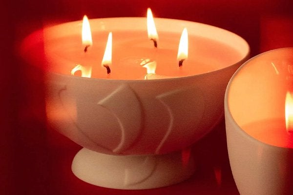 A large 4 wick vyrao candle in the scent Rose Marie, lit with all four wicks alight, shot against a red background.