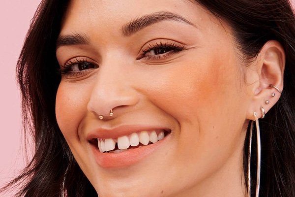 A close up of fair skinned and brunette model wearing a peach make up look in a studio setting with a pink background. 