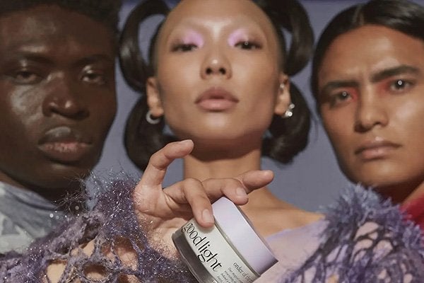 good light moisturiser being held by a female model with a dark skinned model on her left and an asian model to her left shot in a studio with a purple background