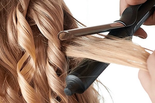 blonde haired model having a section of her hair around the hair wand to curl it.