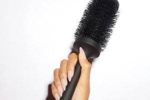 a models hand with pink long nails holding onto a barrelled bristle round brush by ghd against a white background