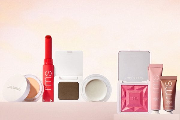 a collection of RMS Beauty products from concealer to a red lip stick dark brown shadow and a soft pink mineral blush placed in a line shot in a studio