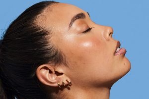 a dark haired model facing to the right with her hair scraped back shot against a blue background