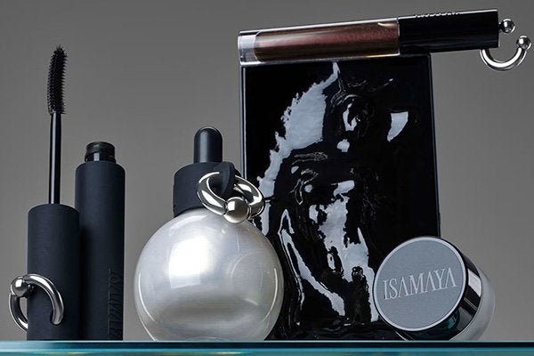Isamaya Beauty Idnsutrial collection featuring a rubberlash mascara, skinlacq circular bottle, a liplacq and a black make up bag shot against a grey background