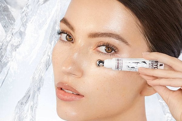 A close-up of a model applying the Charlotte Tilbury Cryo-Recovery Eye Serum under her eyes, with her face next to a block of ice