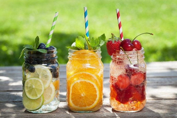 Three lemonade jars with oranges, lime and berries standing on the table. 