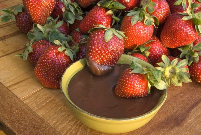 Strawberries laying on the wooden tray with the bowl of liquid chocolate next to it. 