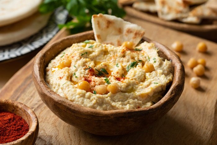 A bowl of hummus on a wooden table surrounded with white bread. 
