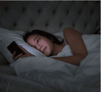 A woman scrolling social media before going to bed.