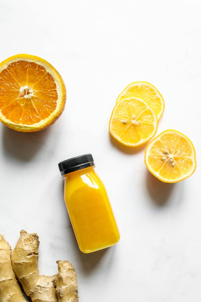 a bottle of ginger drink laid down on a table with slices of orange and a ginger root placed around it.