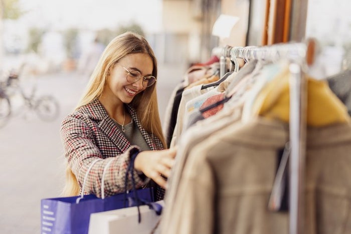 Smiling woman shopping clothes arranged on rack outside store