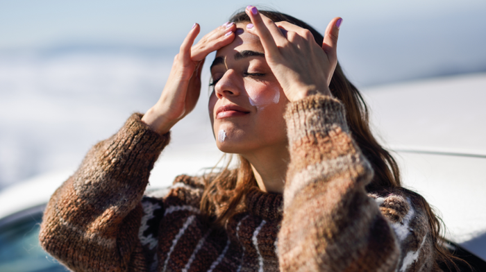 A woman applying moisturiser to her face in winter.