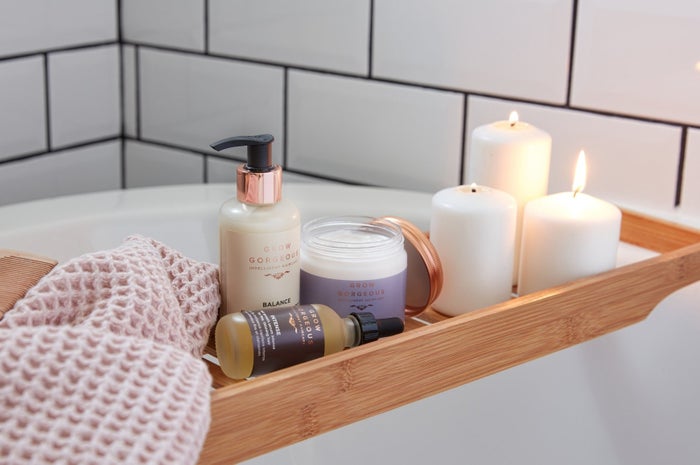 Grow Gorgeous Balance Split Ends Treatment, Intense Hair Growth Serum and Repair Rescue Mask on a bath rack shelf with pillar candles and a pink towel in a bathroom with white subway tiles