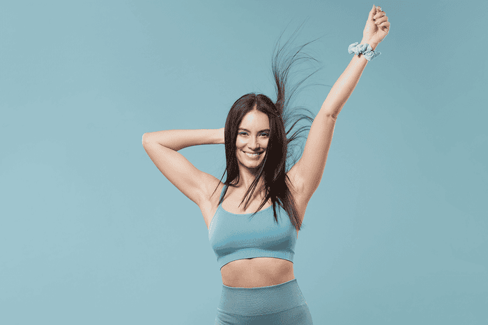 Woman smiling flicking sleek hair, blue background, showing confidence with a hand in the air.